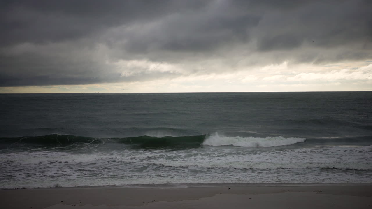 변덕스러운 구름이 지나가는 동안 파도가 해안선에 충돌합니다.