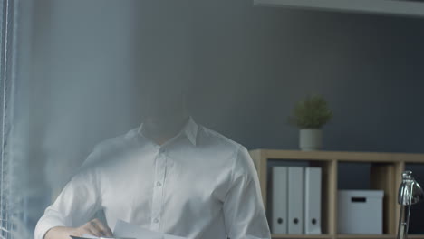 Handsome-Arabian-Businessman-In-White-Shirt-Standing-In-The-Office,-Flipping-Documents-Or-Contract,-Writing-And-Thinking-And-Looking-Out-The-Window