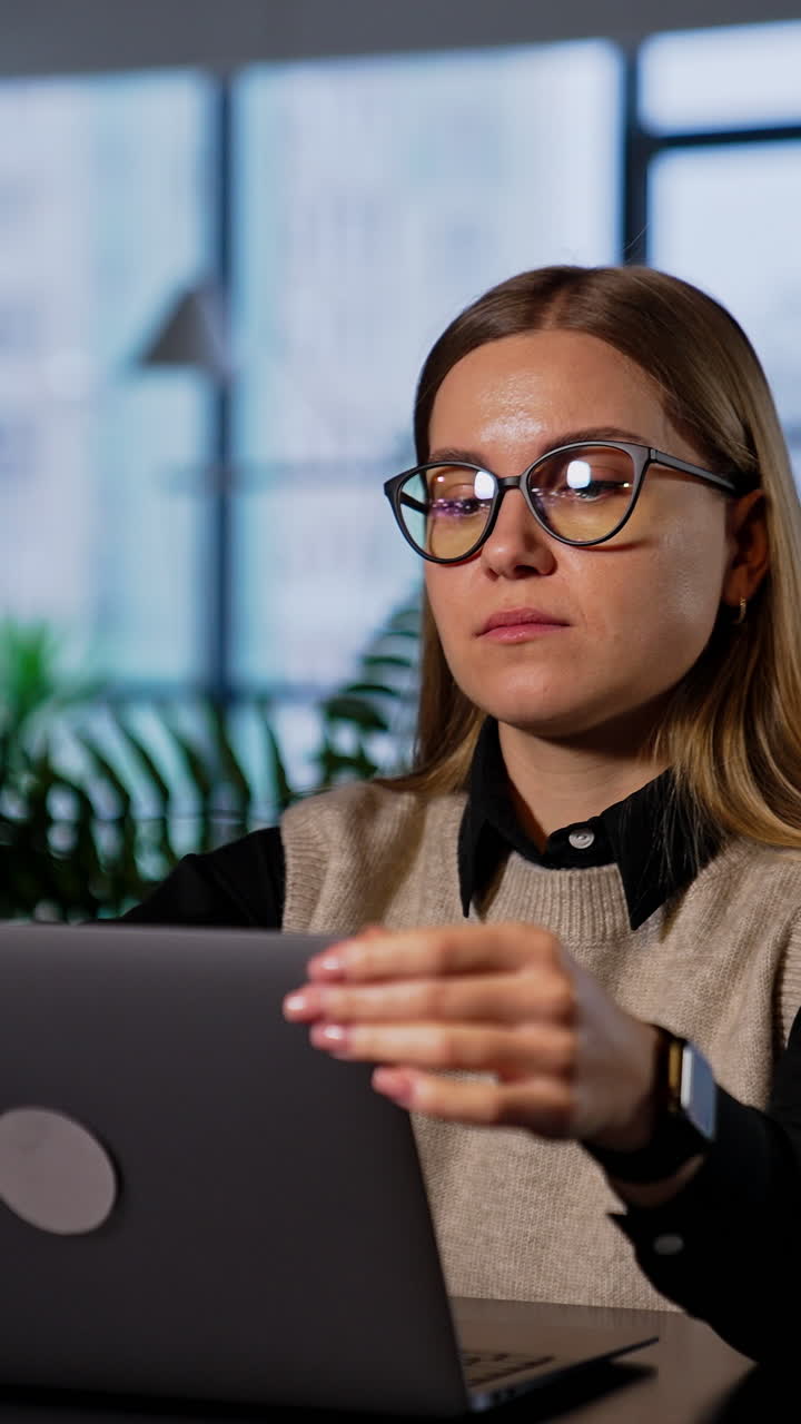Calm pretty woman wearing glasses sits in front of laptop. Lady closes her notebook and takes off her glasses massaging nose bridge. Vertical video