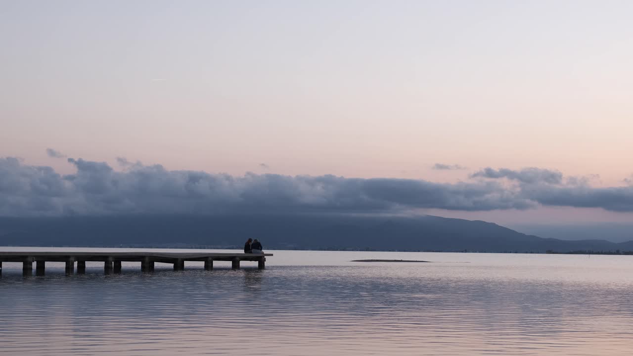 Unrecognizable couple relaxing on quay near sea in evening under sundown sky in summer