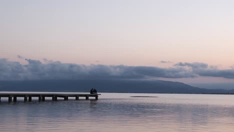 unrecognizable couple relaxing on quay near sea in evening under sundown sky in summer