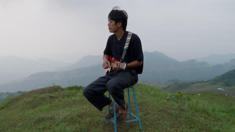 Elegant-classy-asian-male-playing-ukelele-in-slow-motion-in-awesome-exotic-mountain-landscape