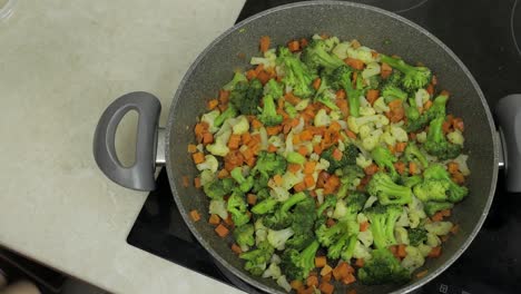 Adding salt to fresh vegetables on frying pan. Carrots, cauliflower, broccoli