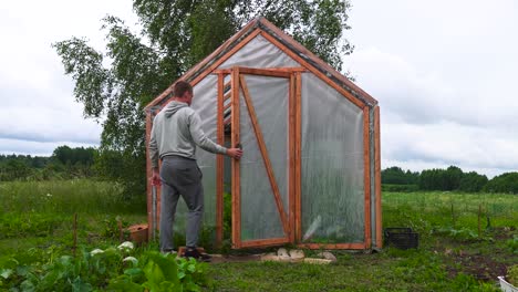 agricultor abre la puerta y camina dentro del invernadero en el jardín de campo, letonia