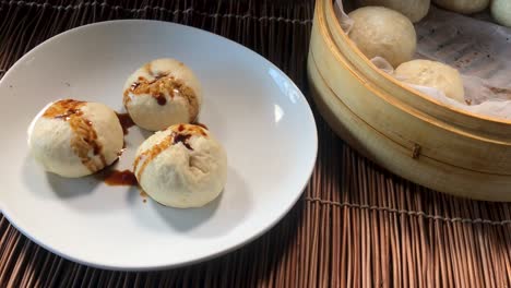 finishing plated steamed buns by adding green onions and soy sauce over buns