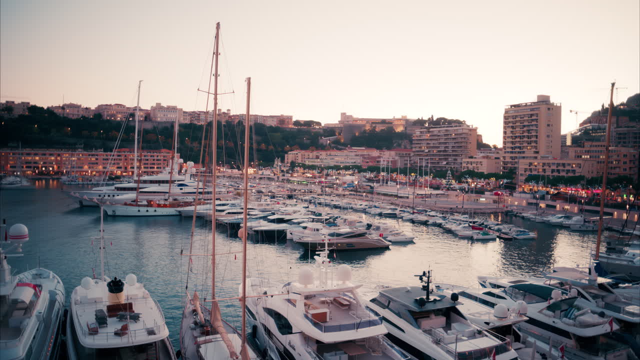 Vista di barche ormeggiate nel porto turistico di Monaco con lo skyline della città sullo sfondo, di sera
