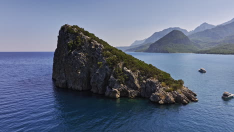 Antalya-Turkey-Aerial-v47-low-level-fly-around-rat-island-surrounded-by-clear-mediterranean-sea-and-green-mountain-landscape-with-boats-cruising-on-the-water---Shot-with-Mavic-3-Cine---July-2022