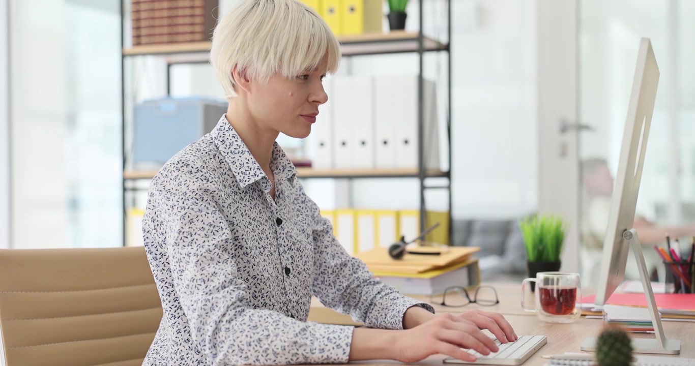 Woman sits at desk with monitor and keyboard working on computer