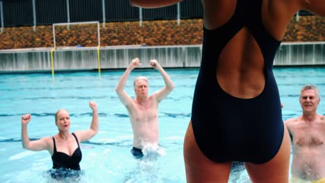Swim-trainer-assisting-seniors-in-performing-exercise