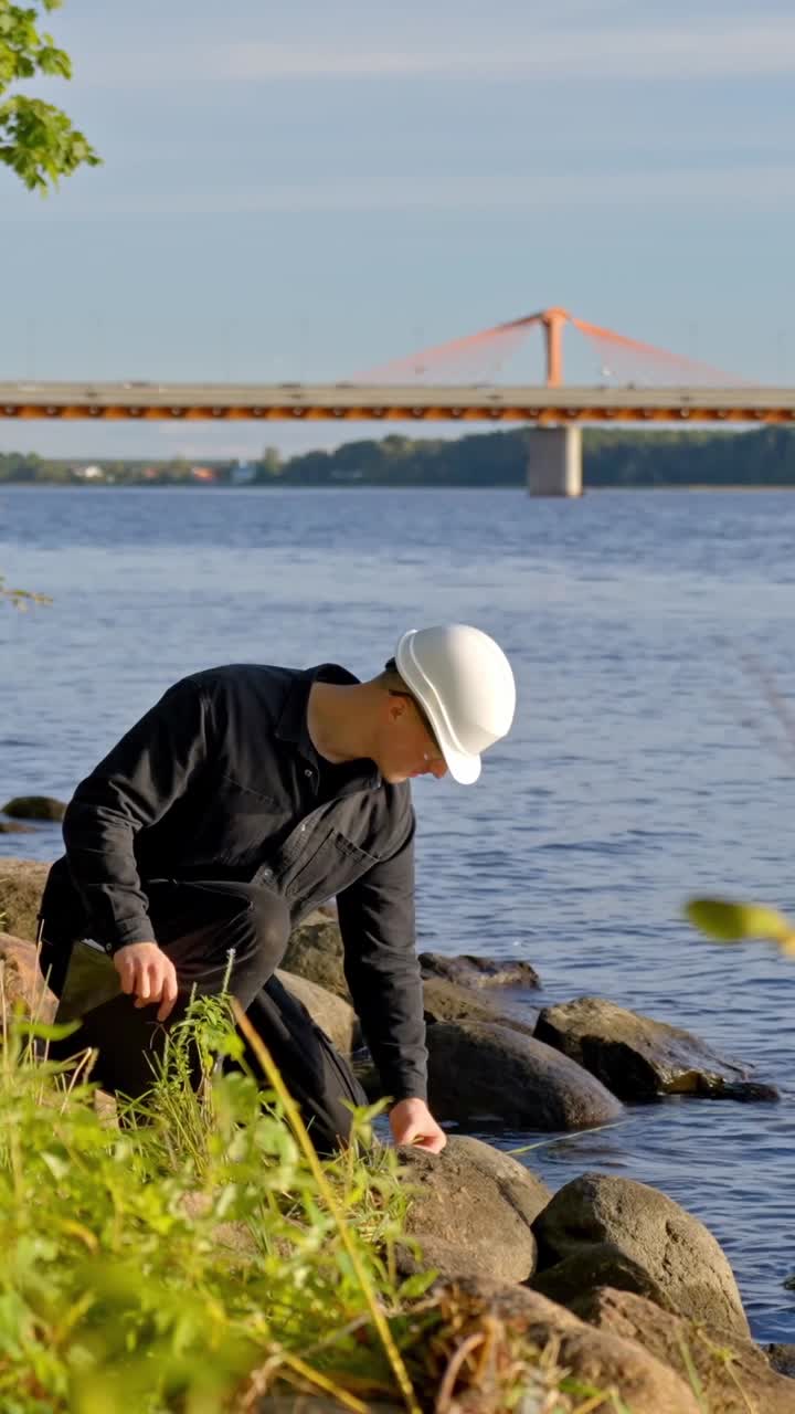 Scientist looks out crouching around near lake edge staring to inspect with clipboard, vertical