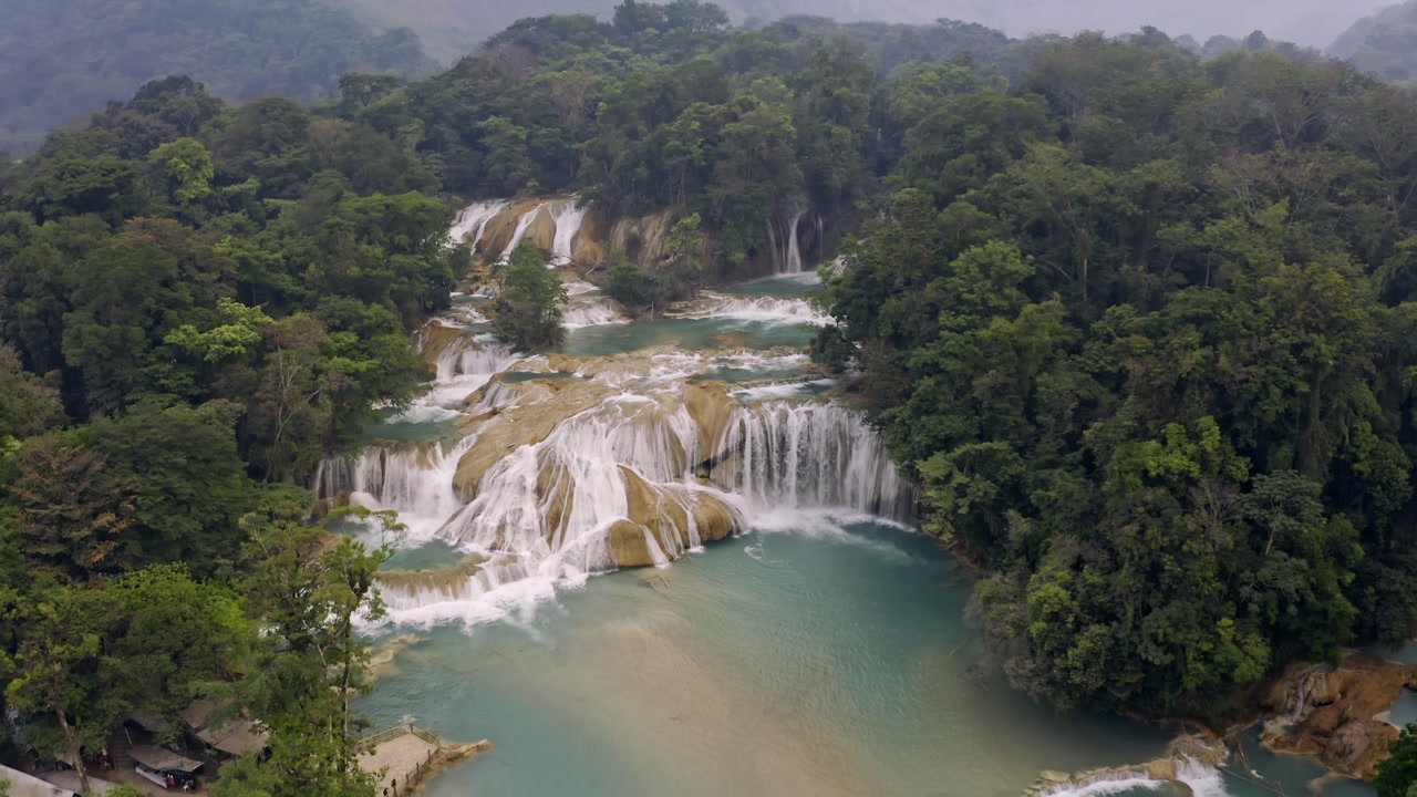 Aerial drone shot of the Agua Azul waterfalls in Chiapas, Mexico. The perspective shows the stunning turquoise water cascading over limestone formations.