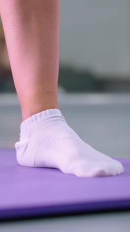 vista de ángulo inferior de primer plano de una persona en estiramiento profundo en una alfombra púrpura con calcetines blancos, centrarse en la postura y la flexibilidad mientras el reflejo borroso suave en el fondo