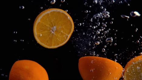 Oranges-Falling-into-Water-Super-Slowmotion,-Black-Background,-lots-of-Air-Bubbles,-4k240fps