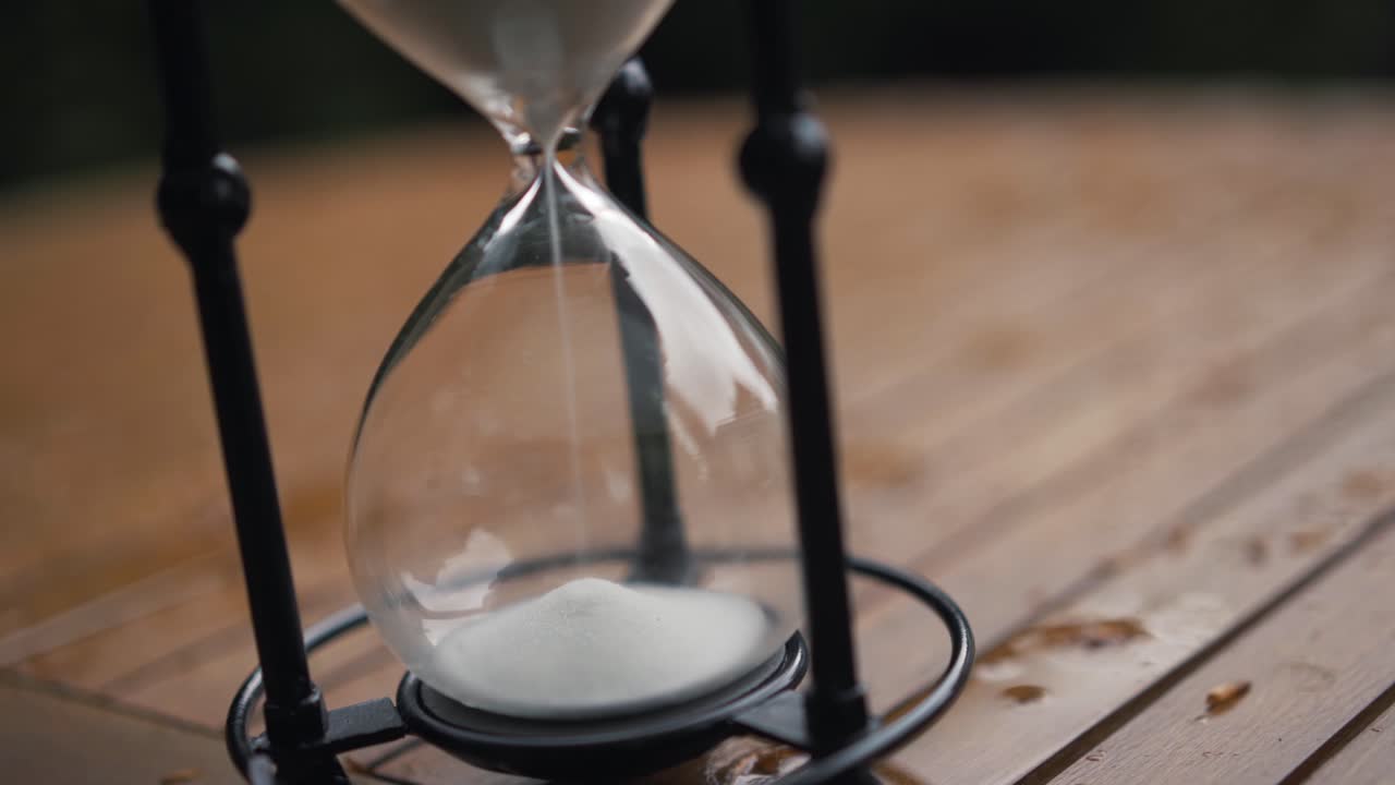 Hour glass on wet garden table white sand running through from top to bottom