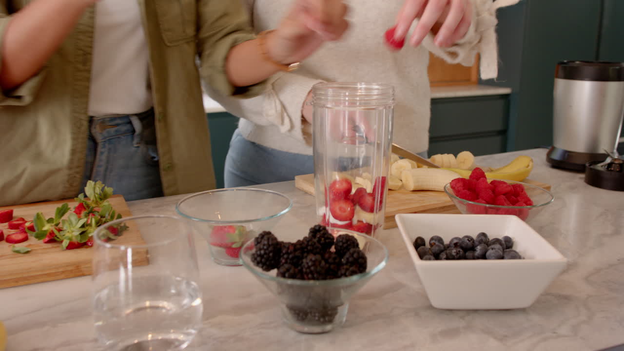 Preparing fresh fruit smoothie, female friends gathering ingredients in kitchen together