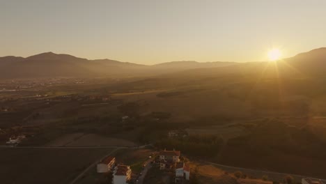 golden sunset over a rural greek valley with scattered houses, distant mountains, and open fields. greece
