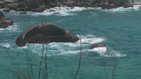 tiro zoom en cámara lenta de olas de agua azul chocando contra una roca en el parque tayrona, colombia