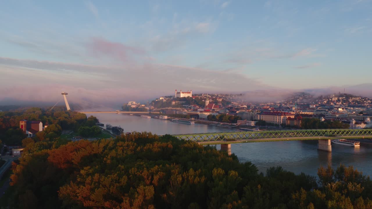 Video aereo cinematografico di Bratislava, in Slovacchia, all'alba con la nebbia che scorre sul Danubio, mettendo in risalto il Ponte UFO e l'iconico Castello di Bratislava immerso nella soffusa luce del mattino