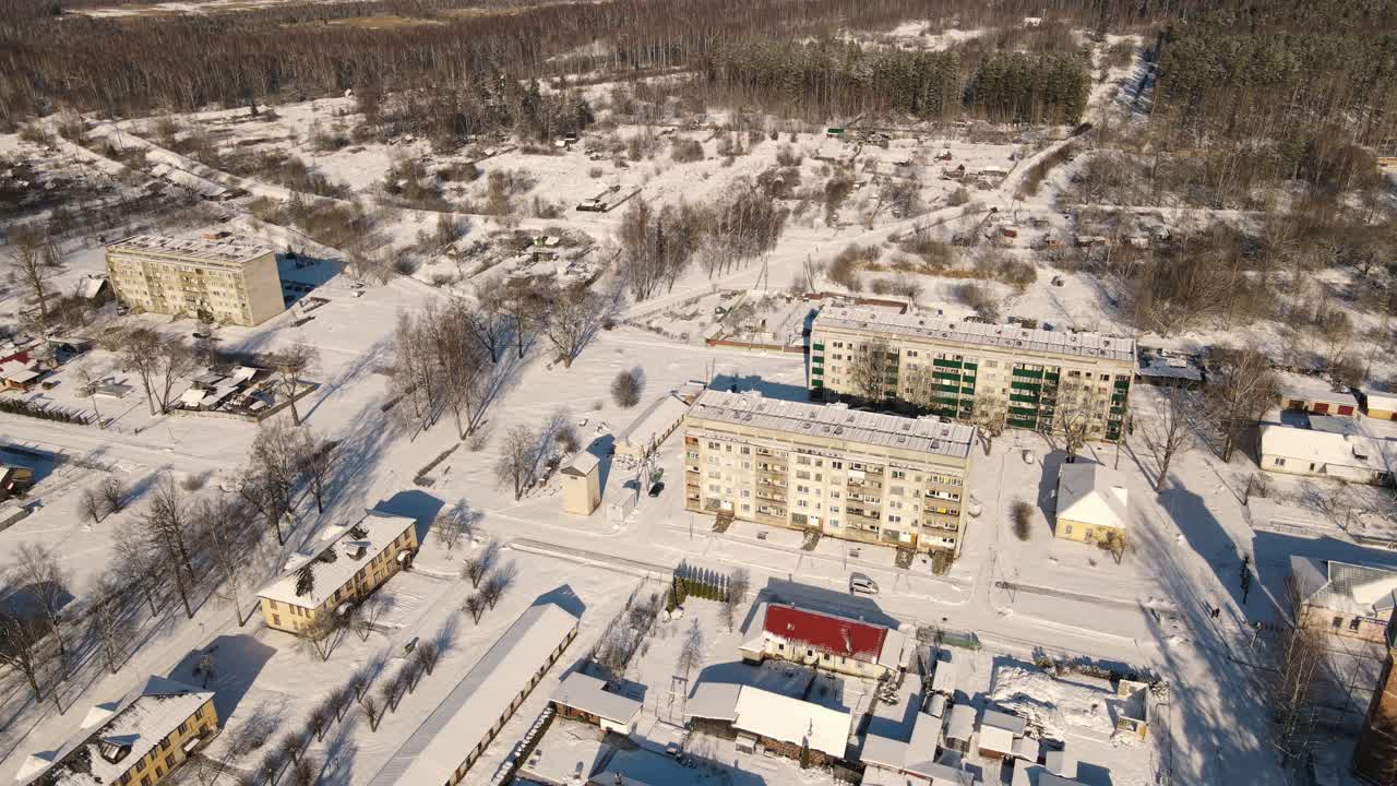 Aerial view of the snow-covered small town of Seda with yellow buildings, streets and roofs covered in white. A peaceful winter landscape in the sunlight.