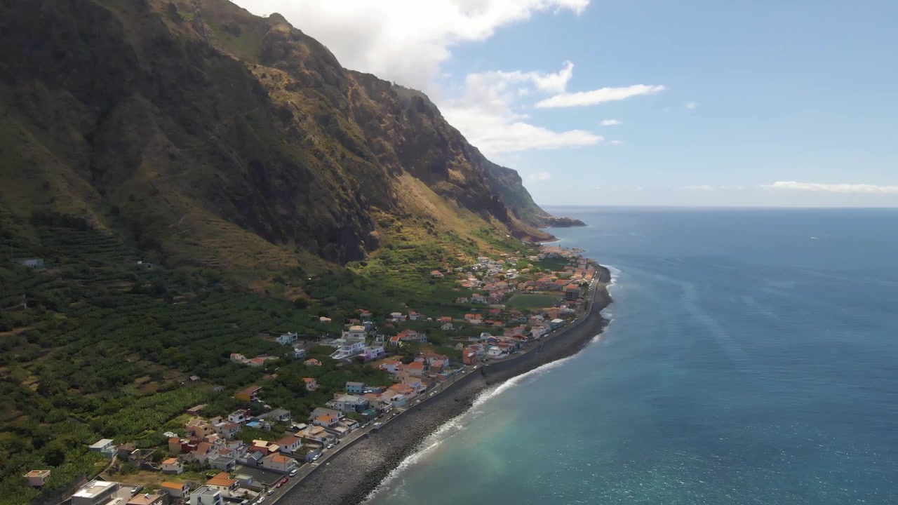 Ripresa aerea che cattura la luce del primo mattino su Paul do Mar, con ombre morbide e condizioni oceaniche calme che creano un'atmosfera pacifica, transizione dalle verdi colline a scogliere costiere drammatiche e all'oceano