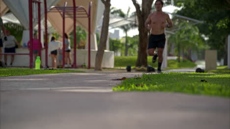 slow motion of a shirtless latin male athlete finishing his running routine towards the camera at the park