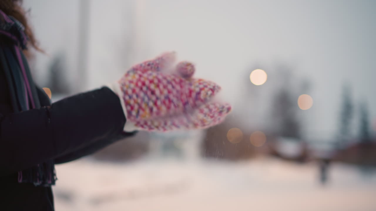 Closeup of colorful knitted mittens clapping outdoors in cold winter snow, snowflakes scattering in air, warm cozy gesture highlighting seasonal atmosphere, handmade texture of winter clothing style