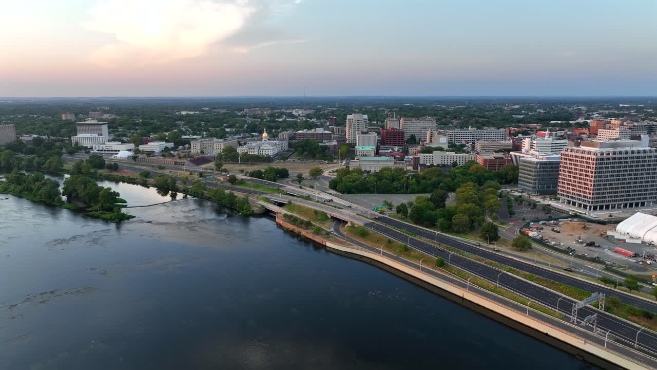 Downtown of Trenton with office buildings, cars on street along Delaware River. Golden sunset in New Jersey, bordering Pennsylvania state. Aerial backwards wide shot