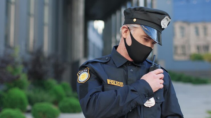 Caucasian policeman wearing protective mask and cap talking on radio in the street