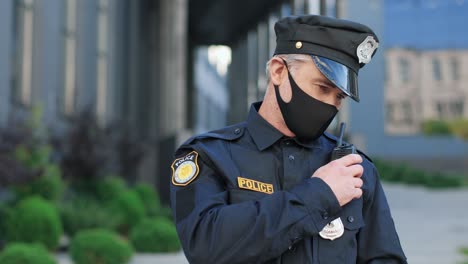 policía caucásico con máscara protectora y gorra hablando por radio en la calle