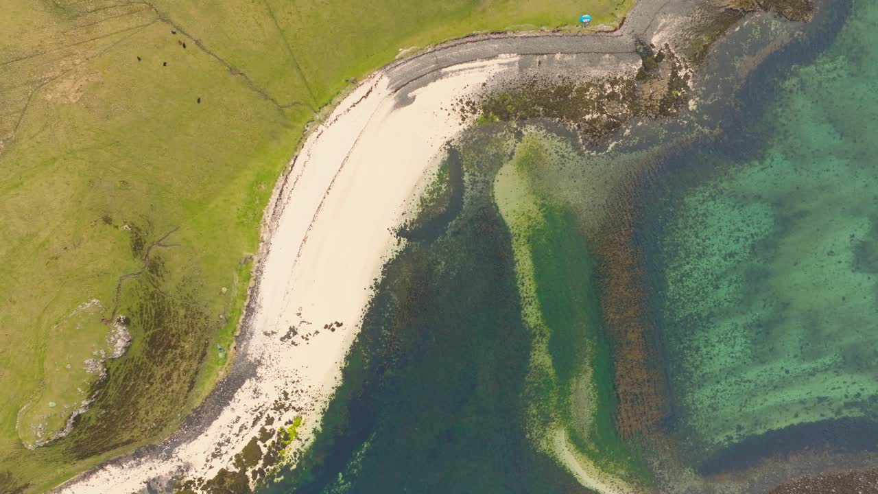 Aerial drone shot of Coral Beach on the Isle of Skye, Scotland, with turquoise waters, white sand, and surrounding green hills creating a stunning coastal landscape