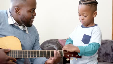 Feliz-Padre-E-Hijo-Afroamericanos-Sentados-En-El-Sofá-Y-Tocando-La-Guitarra,-En-Cámara-Lenta