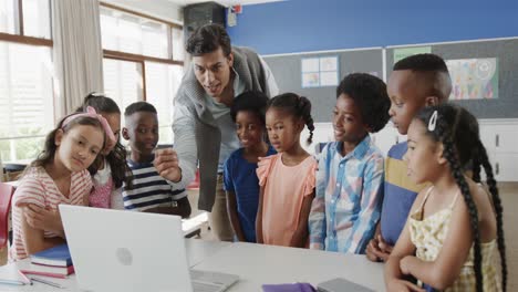 happy diverse male teacher and children using laptop in elementary school class, slow motion