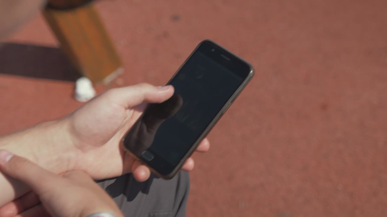 여름 놀이터에서 전화로 소셜 미디어를 탐색하는 청년