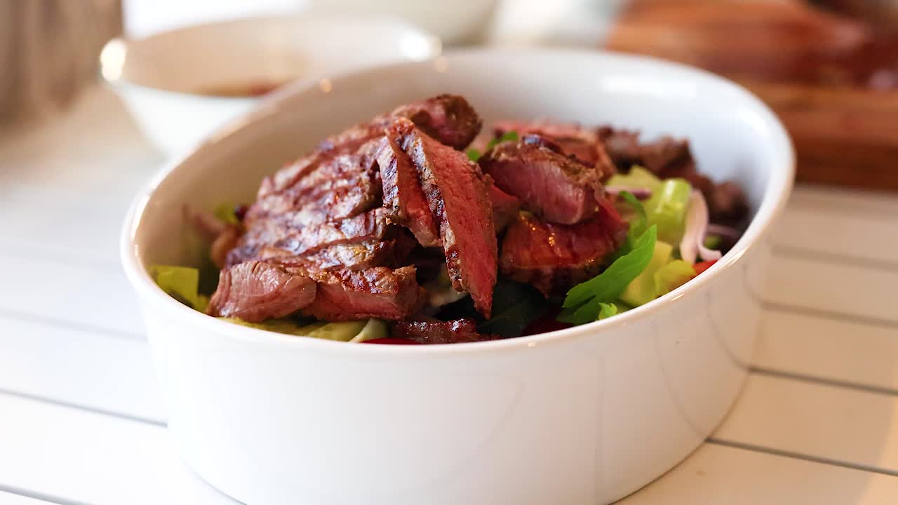 A sequence showing the assembly of a spicy beef salad in a well-lit kitchen setting with fresh ingredients