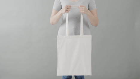 caucasian woman wearing white t-shirt holding white bag on grey background, copy space, slow motion