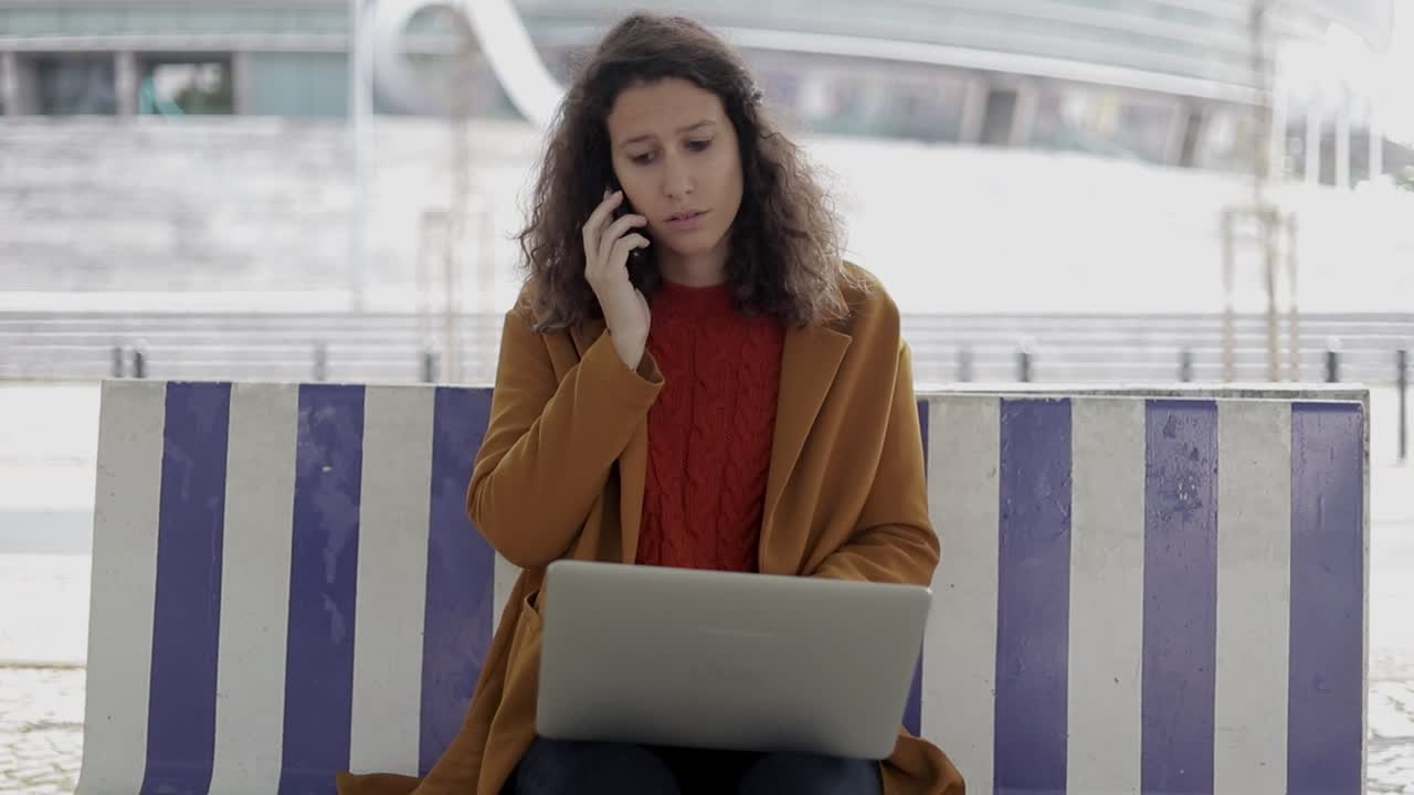 mujer seria usando computadora portátil y hablando por teléfono inteligente