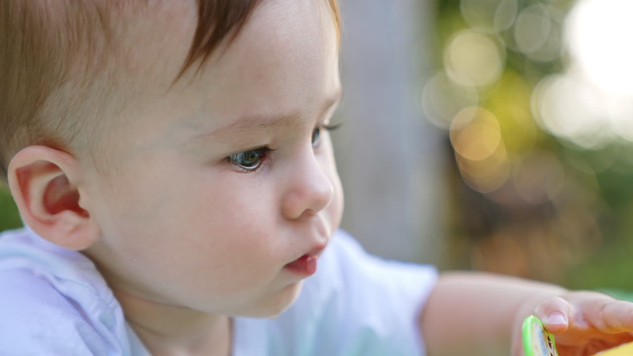 Portrait of an adorable Caucasian baby boy being busy with a toy. Close up. Side view. Blurred backdrop .