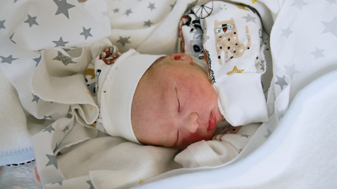 Newborn child sleeping peacefully covered in sheets and blankets. Close up. Adorable Caucasian kid lying on the side. Close up.