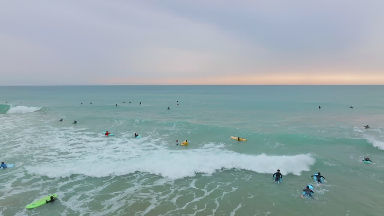 los surfistas en coloridas tablas largas remar a través de la pausa de surf al atardecer