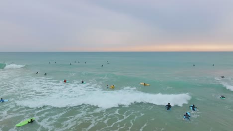 Surfers on colorful longboards paddle out through surf break at sunset