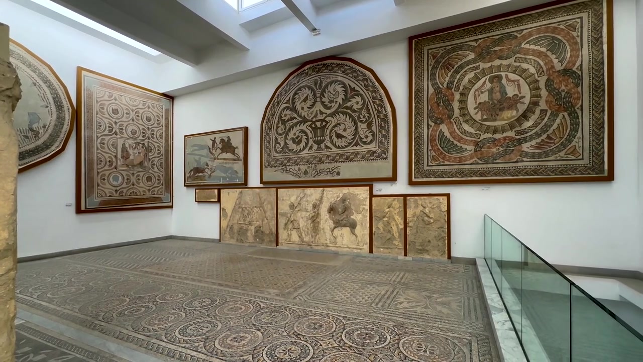 Antichi mosaici romani appesi a pareti bianche sopra grandi mosaici pavimentali nel Museo Nazionale del Bardo. Tunisia