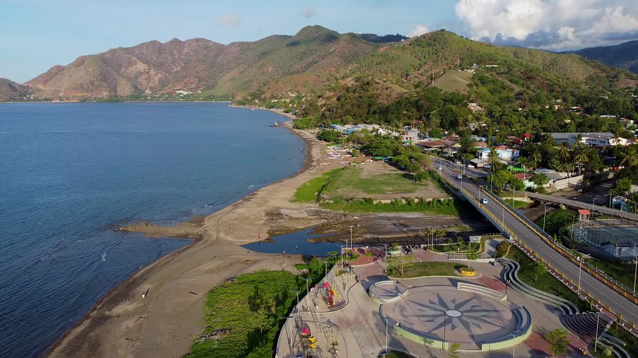Aerial drone rising over children's playground, coastal shoreline, rugged mountainous hilly landscape and blue ocean of capital Dili, Timor-Leste in Southeast Asia
