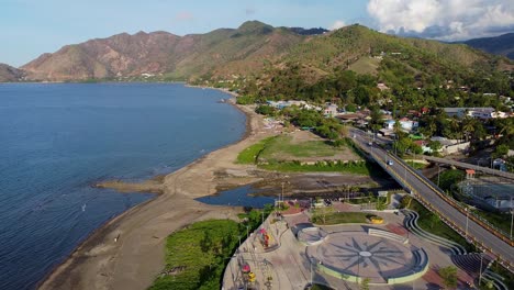 aerial drone rising over children's playground, coastal shoreline, rugged mountainous hilly landscape and blue ocean of capital dili, timor-leste in southeast asia