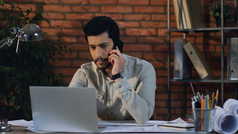 arabian businessman speaking on the phone during working sitting at desk with laptop in the office