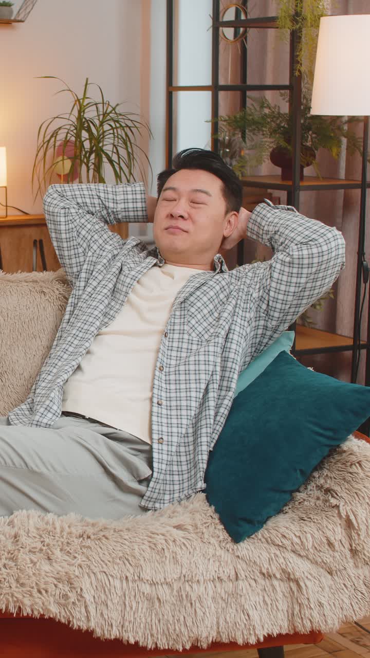행복하고 무모한 중년 중국인 남자가 소파에 편안하게 앉아서 집에서 거실에서 생각하고 있습니다.