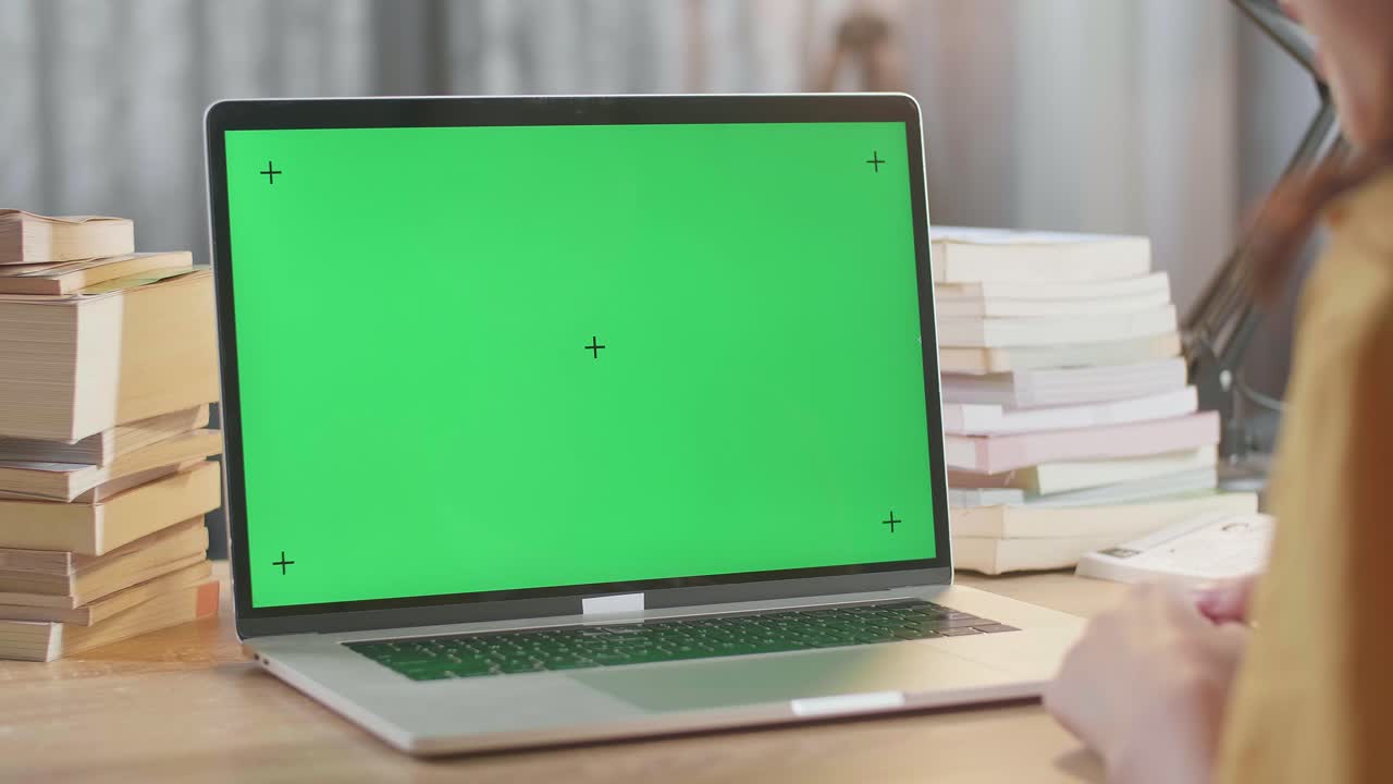 책으로 둘러싸인 녹색 화면의 노트북에서 일하는 사람
