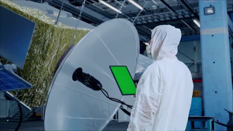vista trasera de científico masculino asiático usar tableta de pantalla verde mientras está de pie con la construcción de la nave espacial