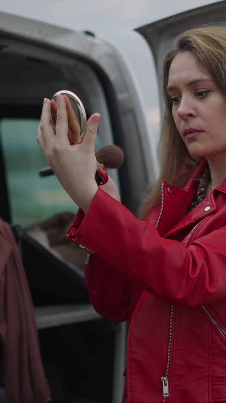 Woman applying makeup in front of a car