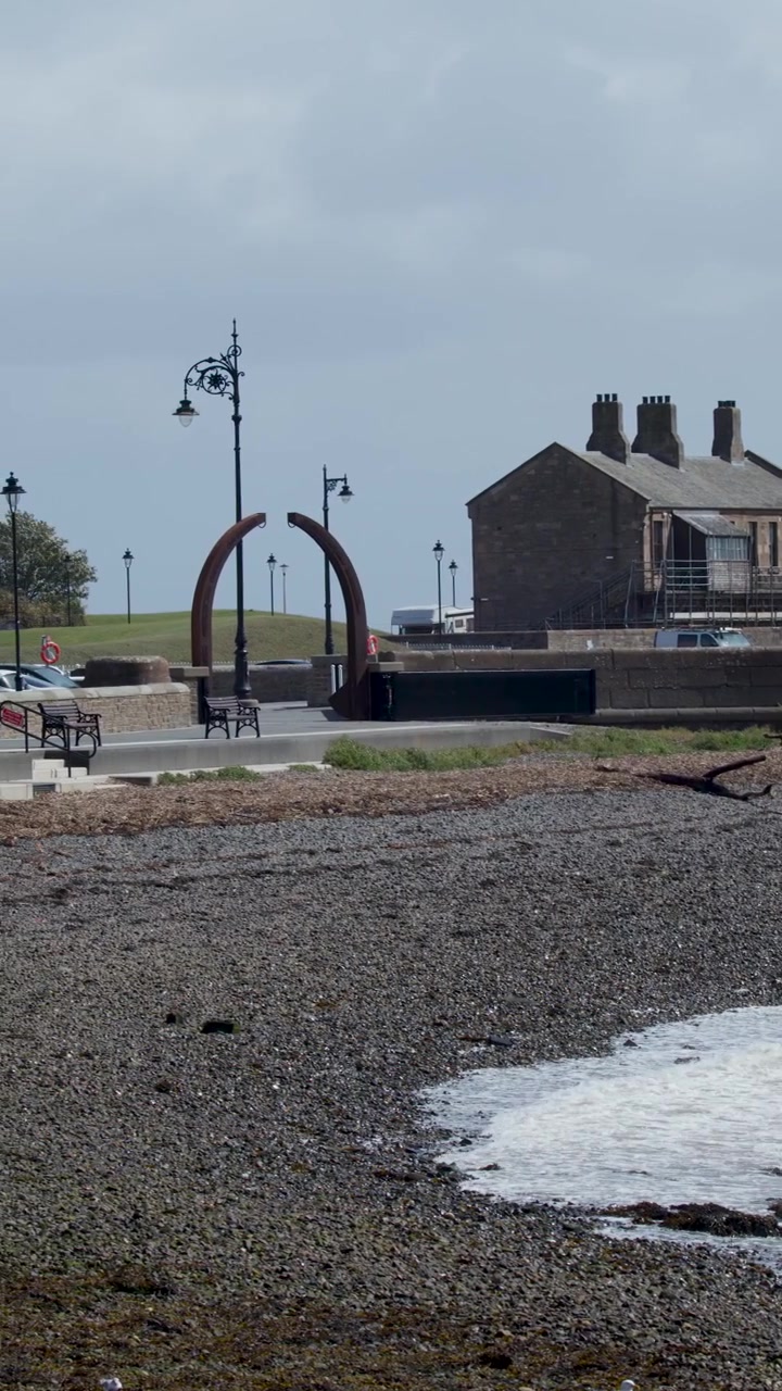 Windy coastal promenade with waves receding, overcast daylight, static wide shot, Broughty Ferry