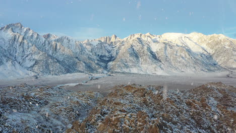 Majestic-view-of-mountain-range-covered-in-snow-during-snowfall,-aerial-fly-backward-view
